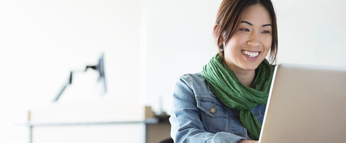 Woman sitting at a desk, smiling at a laptop