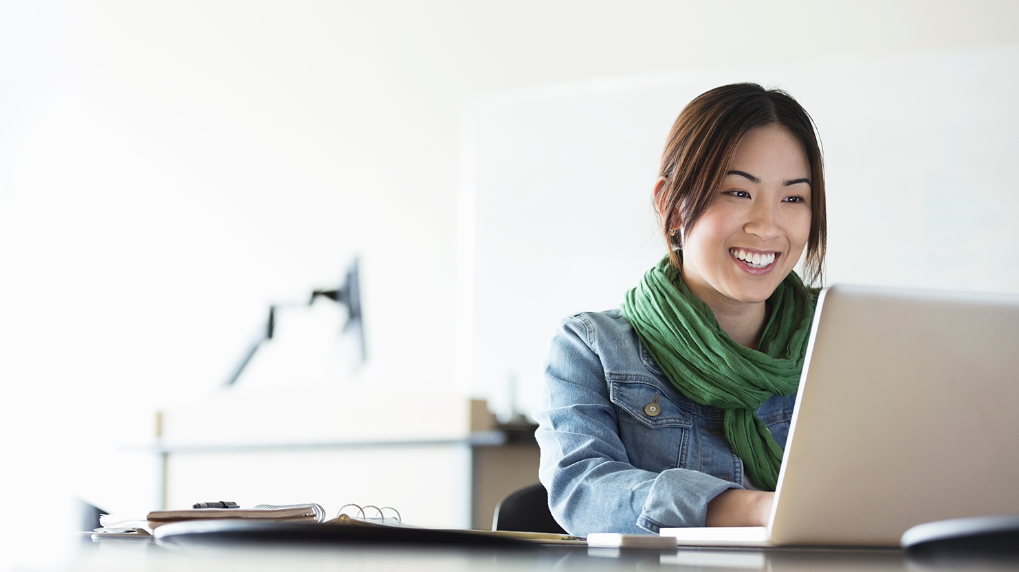 Woman sitting at a desk, smiling at a laptop